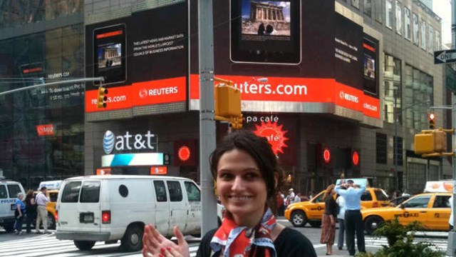 Alina Vandenberghe ở Quảng trường Thời đại (New York), đứng b&ecirc;n dưới một quảng c&aacute;o cho ứng dụng Thomas Reuters iPad do c&ocirc; thiết kế.